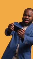 Vertikale afrikanisch amerikanisch Mann spielen Spiele auf Handy im Landschaft Modus, genießen Freizeit Zeit. Spieler genießen Spiel auf Handy, Mobiltelefon Telefon, haben Spaß, Studio Hintergrund, Kamera b video
