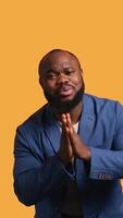 Vertical African american man putting hands together in begging gesture, making wish, isolated over yellow studio background. BIPOC person asking for something, praying and hoping, camera B video