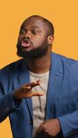 Vertical Annoyed african american man doing shushing hand gesturing, irritated by noise, having negative mood. Person placing finger on lips, doing quiet sign gesture, studio background, camera A video