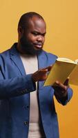 Vertical Man laughing while reading funny book, entertained by engrossing story. Joyful person having fun, being amused by literature novel during leisure time in studio background, camera B video