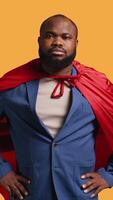 Vertical African american superhero flying with red cape, isolated over studio background, flexing muscles. Man wearing cloak posing as hero in costume showing courage and strength, camera B video