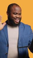 Vertical Cheerful employee greeting coworkers during teleconference meeting using laptop , studio background. Smiling worker waving hand, saluting colleagues during internet call, camera A video