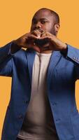Vertical Portrait of jolly friendly african american man doing heart symbol shape gesture with hands. Cheerful nurturing BIPOC person showing love gesturing, isolated over studio background, camera B video