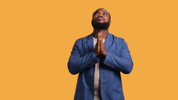 Pious african american man praying to his god, asking for forgiveness. Spiritual BIPOC man doing worship hand gesturing, confessing, begging for pardon, isolated over studio background, camera B video