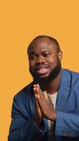 Vertical African american man putting hands together in begging gesture, making wish, isolated over yellow studio background. BIPOC person asking for something, praying and hoping, camera A video