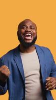 Vertical Portrait of joyful cheerful african american man celebrating, showing positive emotions. Delighted BIPOC person thrilled by achievement, cheering and gesticulating, studio background, camera B video