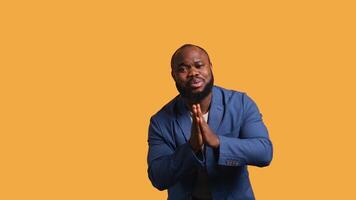 African american man putting hands together in begging gesture, making wish, isolated over yellow studio background. BIPOC person asking for something, praying and hoping, camera B video