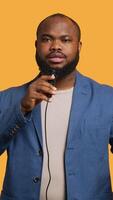 Vertical Portrait of african american lecturer holding monologue using microphone, gesturing with hands, studio background. Expressive BIPOC speaker talking during presentation using mic, camera A video