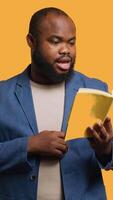 Vertical African american orator reading book aloud, narrating story for audience. BIPOC person presenting literature novel, reciting from pages, entertaining spectators, studio background, camera A video