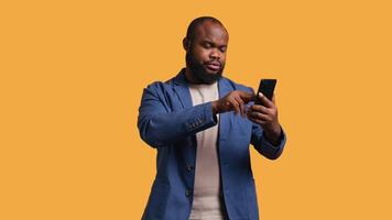 man upprörd efter saknas nödvändig pengar medan påfrestande till köpa grejer uppkopplad på smartphone. ledsen person ser på debitera kort efter få transaktion avvisade på telefon, studio bakgrund, kamera b video