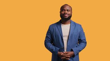 Portrait of cheerful african american man smiling, looking pleased, isolated over yellow studio background. Happy expressive BIPOC person stylishly dressed grinning, feeling satisfied, camera B video