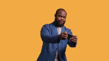 BIPOC person playing games on smartphone, having negative burst of emotions after defeat. Frustrated gamer losing game on phone, isolated over studio background, camera B video