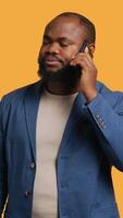 Vertical African american man disagreeing with friend during telephone call, shaking head, studio background. BIPOC person talking on phone with mate, unhappy with proposal, refusing, camera A video