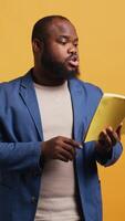 Vertical Man reading book aloud, narrating story for audience. Person enjoying literature novel, reciting from pages, entertaining spectators, isolated over studio background, camera B video