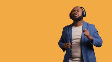 Happy african american person having fun, dancing on rhythm, listening to headphones. Cheerful BIPOC man entertaining himself doing funky movements on music, studio background, camera B video