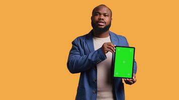 Portrait of african american man doing influencer marketing using green screen tablet, studio background. Smiling BIPOC person holding empty copy space mockup device, camera B video