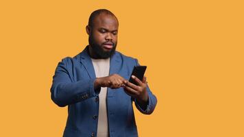 Upbeat man having friendly conversation with friends during teleconference meeting using smartphone, studio background. BIPOC person has fun catching up with mates during online call, camera A video