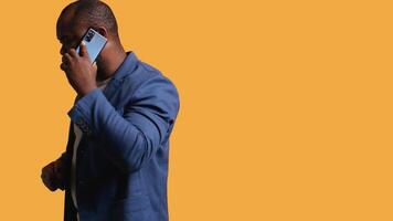 African american man having important phone call with business partner using smartphone, studio background. BIPOC person walking around discussing company matters during telephone call, camera B video