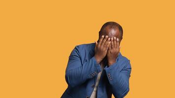 African american man covering face with hands to avoid being recognized, isolated over studio background. Distressed BIPOC person hiding from someone, putting palms in front of face, camera B video