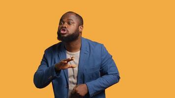 Annoyed african american man doing shushing hand gesturing, irritated by noise, having negative mood. Person placing finger on lips, doing quiet sign gesture, studio background, camera A video