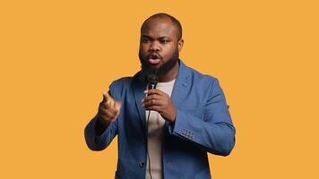 African american motivational speaker holding monologue using microphone, gesturing with hands, studio background. Energetic BIPOC speaker talking during presentation using mic, doing speech, camera A video