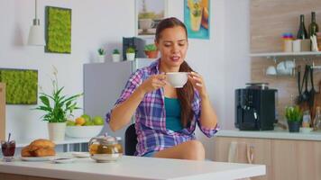 alegre dona de casa bebendo aromático chá às café da manhã. mulher tendo uma ótimo manhã bebendo saboroso natural ervas chá sentado dentro a cozinha sorridente e segurando xícara de chá desfrutando com agradável recordações. video