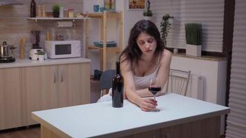 Depressed woman drinking a glass of wine alone in kitchen. Unhappy person suffering of migraine, depression, disease and anxiety feeling exhausted with dizziness symptoms having alcoholism problems. video