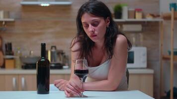 Thoughtful wife looking at a glass of wine sitting on the chair. Unhappy person suffering of migraine, depression, disease and anxiety feeling exhausted with dizziness symptoms having alcoholism problems. video