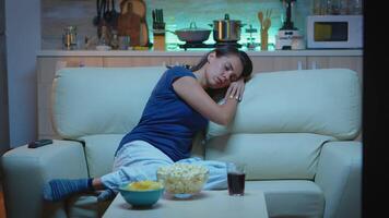 kvinna sovande på en soffa i främre av TV medan tittar på en uttråkad film. trött utmattad ensam sömnig lady i pyjamas faller sovande Sammanträde på mysigt soffa i levande rum, stängning ögon på natt video