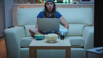 Lady with eye mask having calling on laptop computer at night. Exhausted person in pijamas talking on notebook computer webcam with colleagues sitting on couch at home using internet technology video