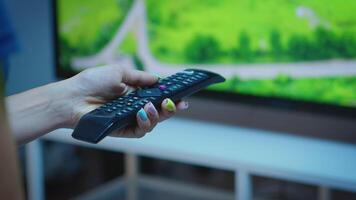 Lady holding TV remote control and pressing the button. Close up of woman hand changing TV channels sitting on comfortable couch in front of television using controller for choosing a movie video