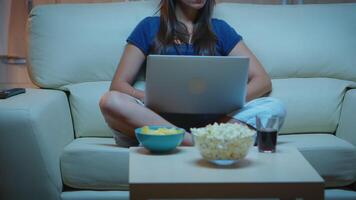 cansado mulher dentro pijamas trabalhando às noite sentado em sofá usando computador portátil. trabalhador autonomo trabalhando dentro frente do televisão lendo escrevendo procurando navegando em caderno usando Internet tecnologia video