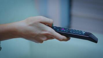 télévision éloigné contrôle dans le mains de femme montrer du doigt à la télé et en changeant canaux. proche en haut de femme en portant manette et pressage le bouton séance sur canapé dans de face de télévision. video