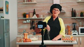 lezione di Farina mentre registrazione cibo preparazione nel casa cucina. pensionato blogger capocuoco influencer utilizzando Internet tecnologia comunicare, tiro blogging su sociale media con digitale attrezzatura video