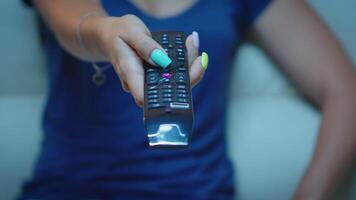 Close up of woman hand changing TV channels sitting on couch. Television remote control in the hands of lady pointing the TV and choosing a movie, holding controller and pressing the button video