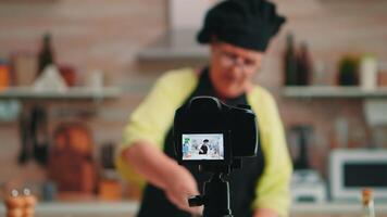 gammal lady bagare presenter mat recept på matlagning podcast från kök. pensionerad bloggare kock influencer använder sig av internet teknologi kommunicera, skytte bloggande på social media med digital Utrustning video