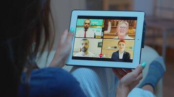 femme écoute en ligne formation sur tablette en retard à nuit séance sur canapé. éloigné ouvrier ayant virtuel réunion consultant avec collègues sur appel et webcam bavarder en utilisant l'Internet technologie. video