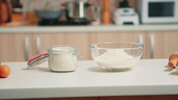 Glass bowl of wheat flour and fresh eggs on table in empty kitchen. Modern dining room equipped with utensils ready for cooking with pastry ingredients for homemade cakes and bread video