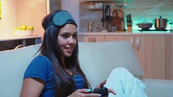 mulher jogador tendo Diversão às casa sentado em sofá jogando jogos atrasado às noite sendo olho mascarar em testa. animado determinado jogador usando controlador joysticks teclado playstation jogos e tendo Diversão ganhando eletrônico jogos video