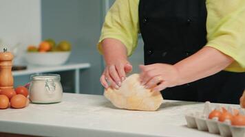 Grandmother hands preparing homemade cookies in modern kitchen kneading on the table. Retired elderly baker with bonete mixing ingredients with wheat flour for baking traditional cake and bread video