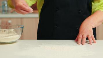 mano diffusione Grano Farina su cucina tavolo superiore per culinario ricetta. pensionato anziano capocuoco con uniforme aspersione, setacciare vagliatura crudo ingredienti di mano cottura al forno fatti in casa Pizza, pane. video