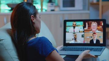 Woman in pijamas lying on sofa using laptop talking about sale report in conference with team. Remote worker having online meeting consulting with colleagues using call and webcam chat video