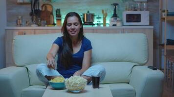 Dame parlant sur caméra séance sur canapé et en mangeant collations. enthousiaste excitation seul femme à la recherche à webcam discuter, socialiser, la mise en réseau avec famille en utilisant l'Internet sur skype dans soir video