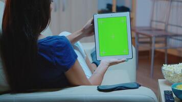 joven dama participación un tableta con verde pantalla sentado en sofá. mujer lectura, mirando a modelo croma llave aislado inteligente cuaderno monitor utilizando tecnología Internet acostado en cómodo sofá. video