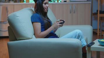 jugador mujer jugando juegos en consola utilizando controlador y palancas de mando sentado en sofá en frente de televisor. emocionado determinado persona relajante juego de azar con inalámbrico controlador teniendo divertido victorioso video