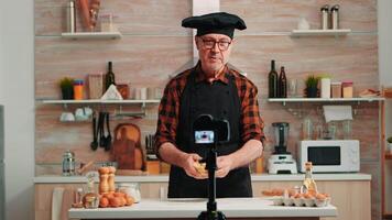 Sénior homme création contenu pour culinaire Blog, expliquant le recette étape par marcher. retraité blogueur chef influenceur en utilisant l'Internet La technologie communicant sur social médias avec numérique équipement video