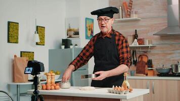 vrolijk ouderen Mens opname de recept stap door stap in schoffel keuken. gepensioneerd blogger chef influencer gebruik makend van internet technologie communiceren, het schieten bloggen Aan sociaal media met digitaal uitrusting video