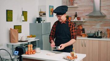 cozinhando dentro frente do profissional Câmera enquanto filmando Novo receita. aposentado blogueiro chefe de cozinha influenciador usando Internet tecnologia comunicar, tiroteio blogging em social meios de comunicação com digital equipamento video