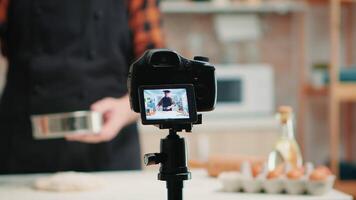 cerca arriba de un cámara rodaje mayor sonriente hombre blogger en cocina cocinando. retirado blogger cocinero hombre de influencia utilizando Internet tecnología comunicado en social medios de comunicación con digital equipo video