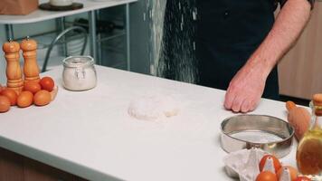 Hands of chef man sifting flour on dough for baking. Elderly senior baker with bonete and uniform sprinkling, sieving, spreading rew ingredients by hand cooking homemade pizza and bread. video